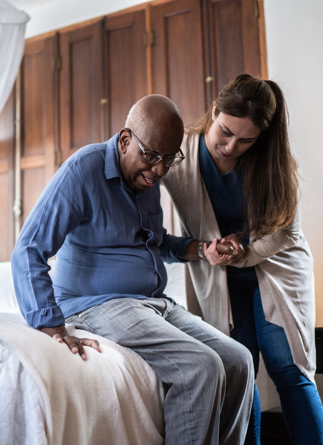 A certified PAS caregiver assists a patient getting off of their bed